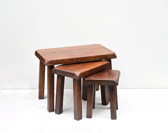 Puede incluir: Juego de tres taburetes apilables de madera. Los taburetes son de madera marrón oscuro con veta natural. Cada taburete tiene una parte superior rectangular y cuatro patas resistentes. Diseñados para encajar uno dentro del otro.