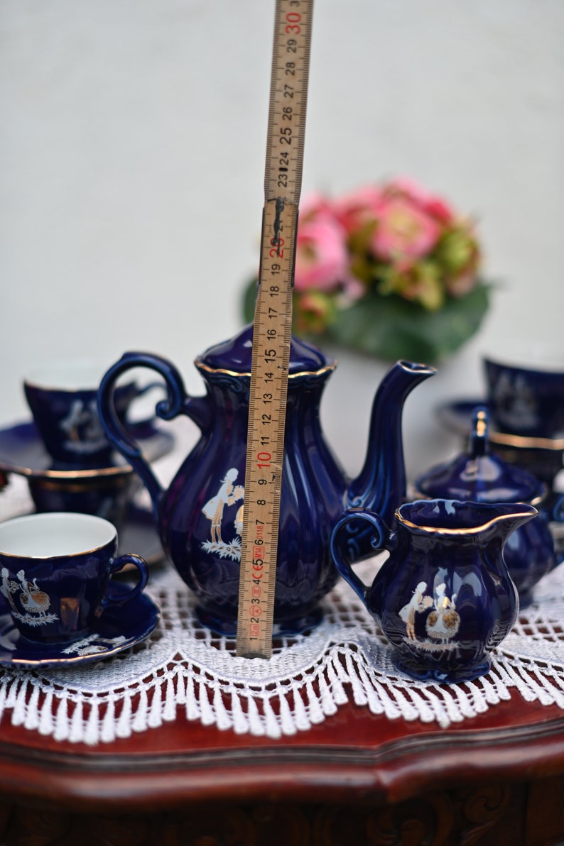 May include: A blue and gold porcelain tea set with a floral design. The set includes a teapot, creamer, sugar bowl, and two teacups and saucers.
