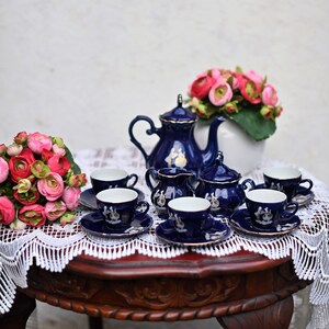 May include: A blue and white porcelain tea set with a teapot, creamer, sugar bowl, and six cups and saucers. The set is arranged on a wooden table with a white lace tablecloth.