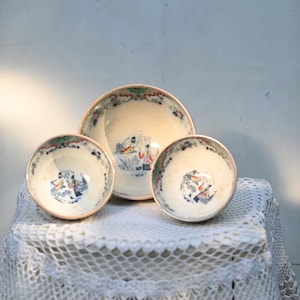 Könnte beinhalten: Drei weiße Keramikschalen mit blauen und roten Blumendesigns. Die Schalen sind ineinander verschachtelt auf einer weißen Häkeltischdecke.