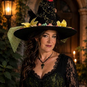 May include: A black sequined witch hat adorned with a white feather, a red flower, and yellow floral accents. The hat features a wide brim with a light green mesh fabric draped on one side. The hat is worn with a black lace dress and a black belt.