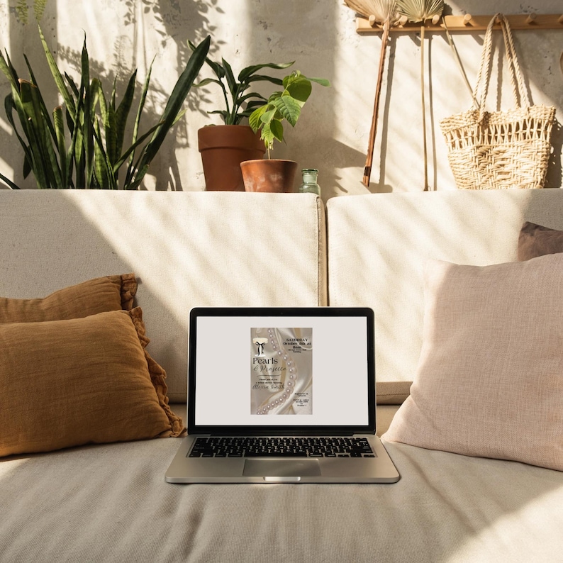 May include: A laptop computer with a white background on the screen. The screen shows a digital invitation with the text "Pearls & Magnolia" and a pearl necklace with a bow.