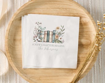 May include: White paper napkin with a watercolour illustration of a stack of books with flowers and the text "A new chapter begins The Johnsons".