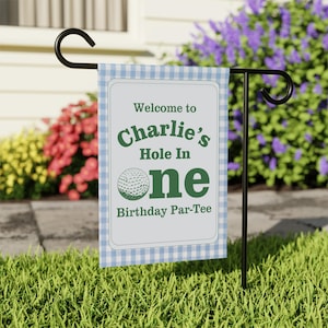Peut inclure: Un drapeau de jardin à carreaux bleus et blancs avec le texte "Welcome to Charlie's Hole In One Birthday Par-Tee" en vert. Le drapeau présente un motif de balle de golf et est sur un support en métal noir.
