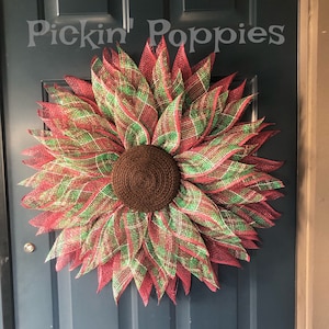 May include: A red and green plaid sunflower wreath with a brown center. The wreath is hanging on a dark blue door. The text "Pickin' Poppies" is visible on the door.