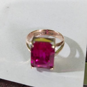 May include: A gold ring with a large, rectangular, dark pink gemstone. The ring is inscribed with "SIBLENG 585".