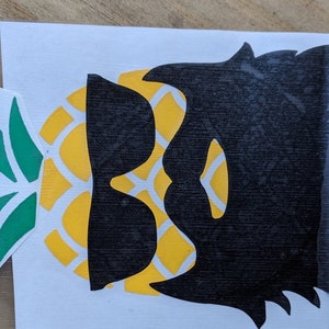 May include: A black silhouette of a person wearing sunglasses with a yellow pineapple pattern behind the head.