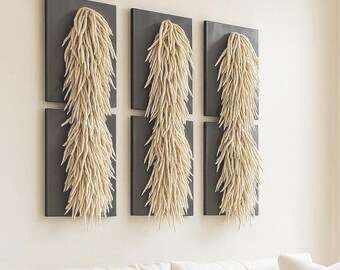 May include: A living room scene featuring a white sofa with a textured beige pillow and a round coffee table. Above the sofa, three sets of wall art with dark gray backgrounds and beige, textured, vertical elements are displayed.