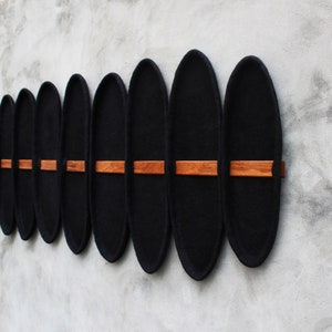 May include: A series of black, oval-shaped wall decor pieces with a wooden accent. The pieces are mounted on a gray wall, creating a modern and minimalist aesthetic. The wooden accents are rectangular and positioned horizontally.