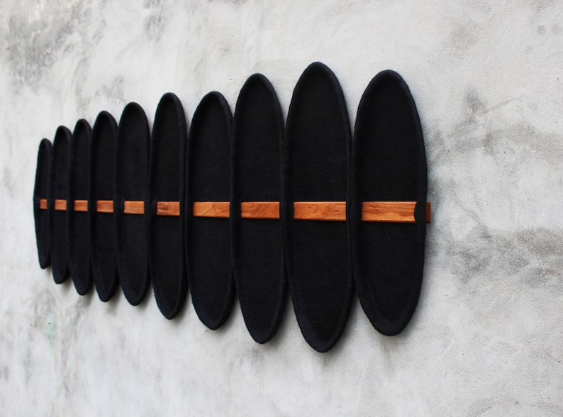 May include: A series of black, oval-shaped wall decor pieces with a wooden accent. The pieces are mounted on a gray wall, creating a modern and minimalist aesthetic. The wooden accents are rectangular and positioned horizontally.