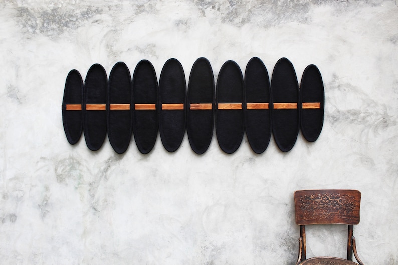 May include: A wall-mounted decorative piece featuring eleven black, oval-shaped elements. Each element has a horizontal, rectangular wooden accent. The piece is mounted on a textured, light gray wall. A vintage wooden chair is in the foreground.