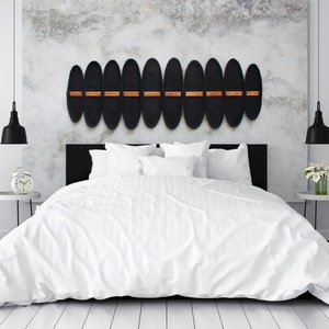 May include: A modern bedroom with a white bed, pillows, and bedding. Above the bed is a decorative wall piece with black oval shapes and wooden accents. Black pendant lights hang on either side of the bed. A white alarm clock and flowers sit on side tables.