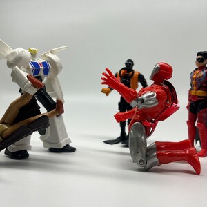 May include: A group of five action figures, including a white robot, a red and silver robot, a black and orange robot, a brown and tan figure, and a red, black, and blue figure. The figures are posed in a fighting stance.