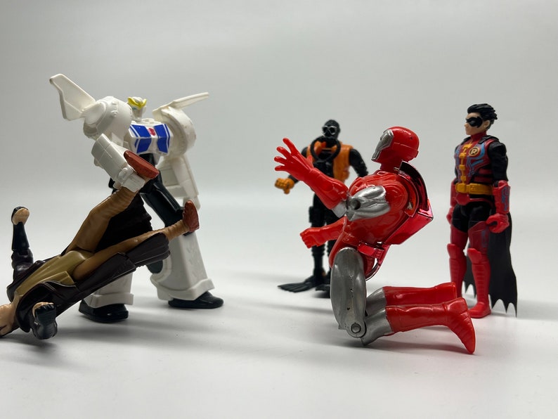 May include: A group of five action figures, including a white robot, a red and silver robot, a black and orange robot, a brown and tan figure, and a red, black, and blue figure. The figures are posed in a fighting stance.
