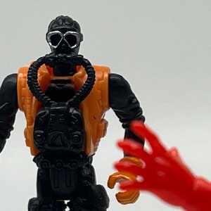 May include: A black and orange action figure wearing a diving mask and a scuba tank. The figure has a black diving suit and a black and orange scuba tank. The figure is holding a black scuba tank.