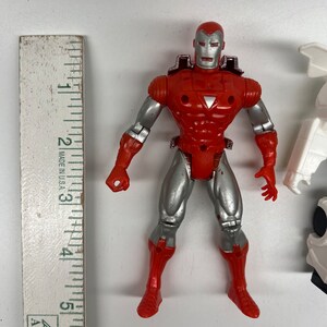May include: Red and silver action figure of Iron Man, a superhero from Marvel Comics. The figure is approximately 5 inches tall and has a detailed sculpt.