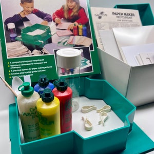 May include: A green plastic tray with a white surface and a set of four colorful bottles with green lids. The bottles are labeled "Galt Wash Pulp", "Galt Colour", "Galt Colour", and "Galt Colour". The tray also contains a set of white plastic clips. The tray is part of a paper making kit.