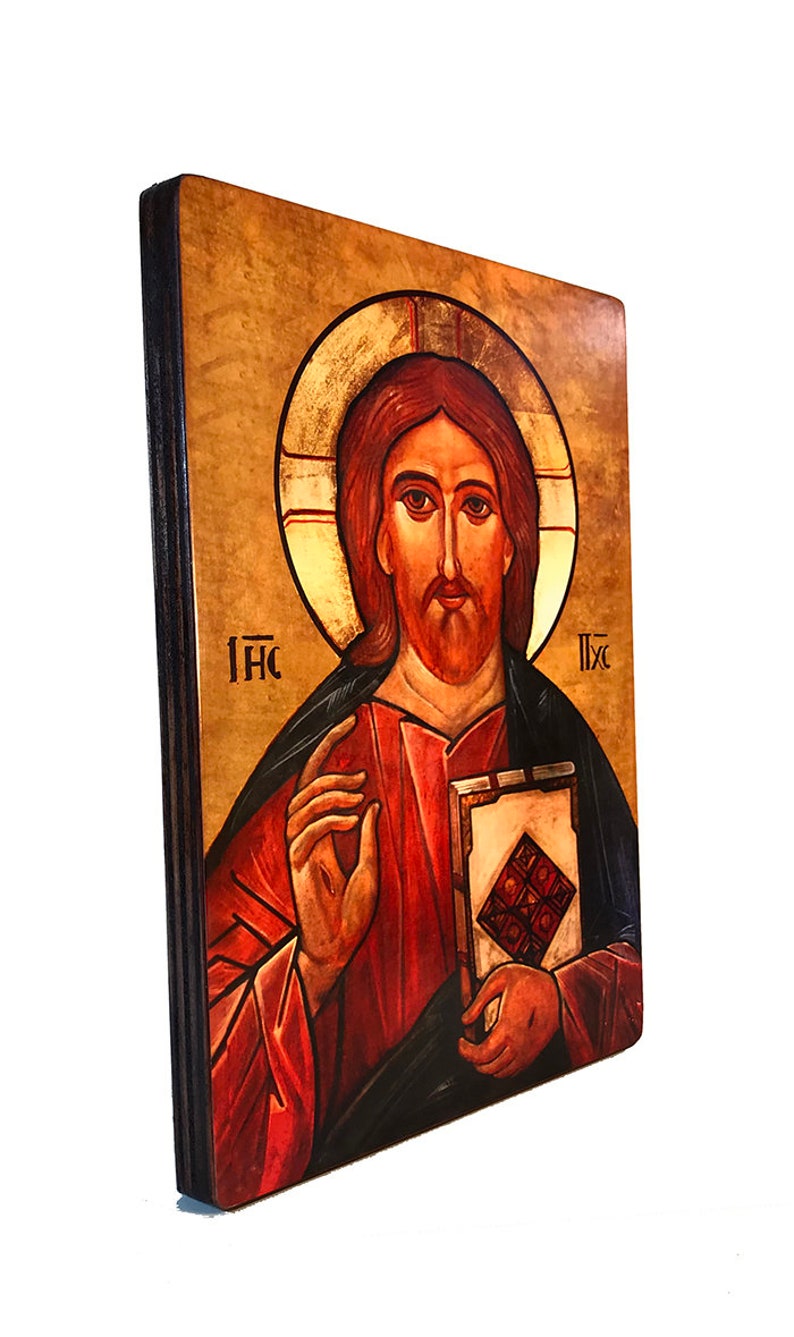 May include: A hand-painted icon of Jesus Christ on a wooden panel. The icon depicts Jesus with a red robe and a book in his hand. The background is a golden color with a halo around Jesus' head. The text "IHC" is written on the left side of the icon and "IXC" is written on the right side.