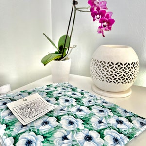 May include: A white fabric tote bag with a floral print of white anemones on a green background. The bag has a white tag with the text "Laurel Co." printed on it.