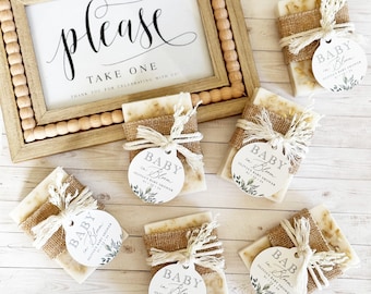 May include: Six small bars of soap wrapped in burlap and tied with twine. Each bar has a round tag attached with the text "Baby in Bloom" and a floral design. The tags are white with black text and green floral accents.