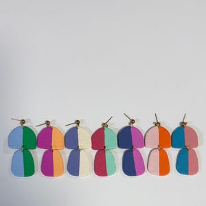 May include: Seven pairs of dangle earrings featuring a two-part design with a semi-circle top and a rounded bottom piece. Each earring is split into two distinct colors, including combinations of blue, green, purple, orange, pink, and cream.