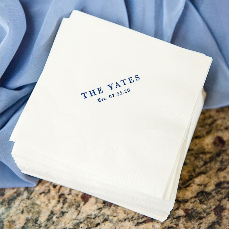 May include: A stack of white paper napkins with a blue imprint that reads "THE YATES Est. 07.25.20"