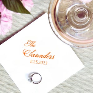 May include: White napkin with the text "The Saunders 11.25.2023" in orange script. A silver ring is on the napkin.