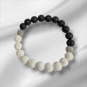 May include: A black and white lava rock bracelet with two silver spacer beads. The bracelet is made of round beads and is approximately 18 cm in length.