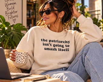 以下が含まれることがあります： 胸元に黒い文字で「the patriarchy isn't going to smash itself」とプリントされたクリーム色のクルーネックトレーナー。長袖でリブ編みのネックラインが特徴の、柔らかい生地で作られたリラックスフィットの衣類です。