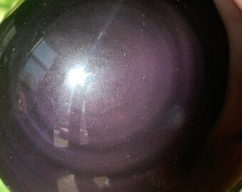 May include: A dark purple obsidian sphere with a reflective surface. The sphere has a swirling pattern of light and dark shades.