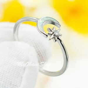 May include: A silver ring with a crescent moon and a star design. The moon is set with a light green opal stone.