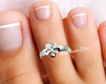 May include: Silver toe ring with a flower design. The ring is on a person's toe.