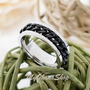 May include: A silver and black chain ring with a spinning band. The ring is sitting on a green woven ball.