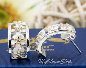 May include: A pair of silver hoop earrings with white flower accents and gold accents. The earrings are on a blue background.