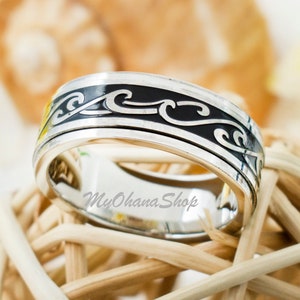 May include: A silver ring with a black wave design. The ring is on a woven straw background.