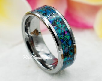 May include: A silver-colored ring with a band of blue, green, and purple iridescent material. The ring is set against a backdrop of white and colorful flowers, creating a vibrant and eye-catching display. The ring is a piece of jewelry.
