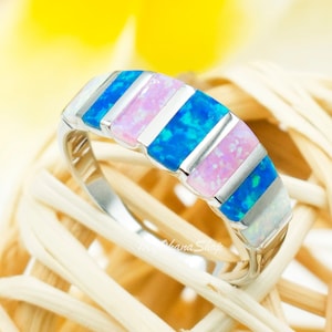 May include: A silver band ring with alternating blue, pink, and white opal stones.