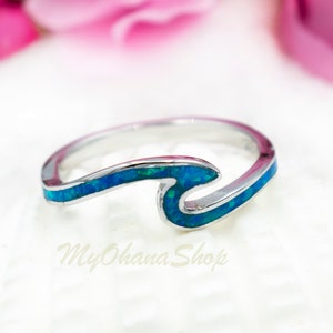 Könnte beinhalten: Ein silberner Ring mit einem blauen Opal-Wellendesign. Der Ring liegt auf einem weißen Hintergrund.