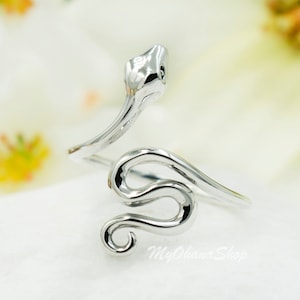 Peut inclure: Une bague en argent en forme de serpent avec un corps enroulé et une tête relevée. La bague est ouverte et réglable.