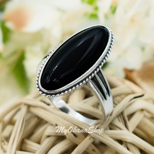 May include: A silver ring with a black oval gemstone. The ring has a beaded edge around the gemstone and a simple band.