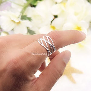 May include: A silver ring with a woven design. The ring is worn on a finger.