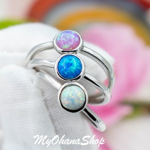 May include: Three silver rings with opal stones. The top ring has a pink opal, the middle ring has a blue opal, and the bottom ring has a white opal.