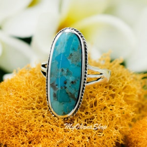 May include: A silver ring with a turquoise oval stone set in a bezel setting. The ring has a delicate design with a twisted band.
