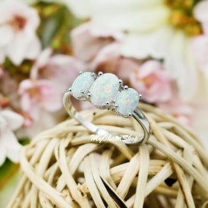 May include: A silver ring with three oval-shaped white opals. The ring is set on a woven background.
