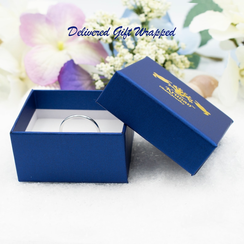 May include: A silver ring in a blue gift box with a gold logo that says "Aubrey" and "Classic Jewelry". The box is open and the ring is sitting inside. The text "Delivered Gift Wrapped" is written in white on a pink and white floral background.