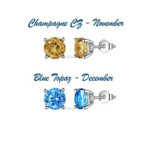 May include: Two pairs of silver stud earrings with round gemstones. The top pair features champagne colored cubic zirconia stones and the bottom pair features blue topaz stones. The text "Champagne CZ - November" and "Blue Topaz - December" is displayed above each pair of earrings.