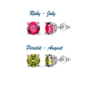 May include: Two pairs of silver stud earrings with birthstone gems. The first pair features a red ruby, representing July. The second pair features a green peridot, representing August.