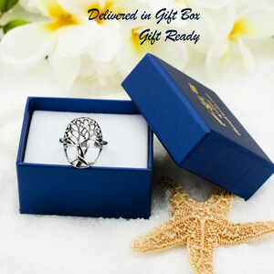 May include: A silver tree of life ring presented in a blue gift box. The ring has an openwork tree design. The box is open, showing the ring against a white interior. The text "Delivered in Gift Box, Gift Ready" is visible.