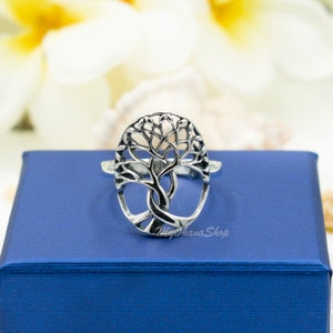 May include: A silver ring with a tree of life design. The ring has an openwork tree design, set against a blue background. The ring is a piece of jewellery.