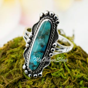 Könnte beinhalten: Ein silberner Ring mit einem Türkis-Stein, der in einem detaillierten ovalen Design gefasst ist. Der Ring hat einen seilartigen Rand und einen gewellten Rand.